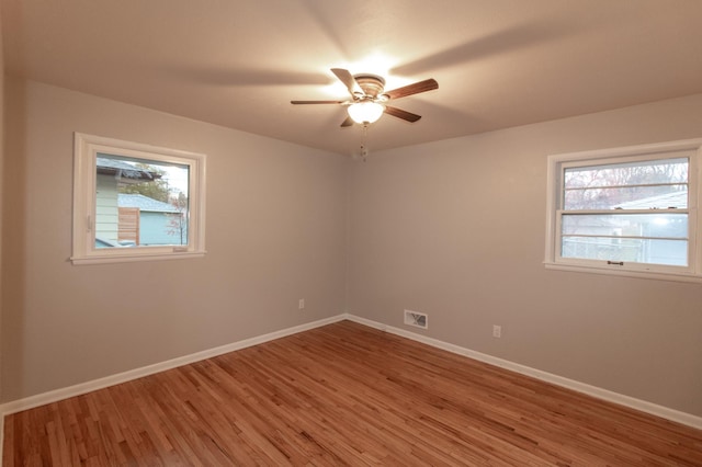 empty room with light wood-type flooring, a ceiling fan, visible vents, and baseboards