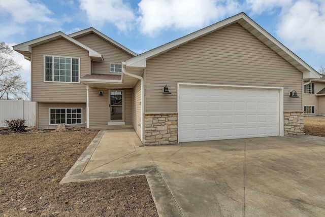 tri-level home featuring a garage, stone siding, concrete driveway, and fence