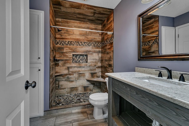 bathroom with tiled shower, toilet, vanity, and a textured ceiling