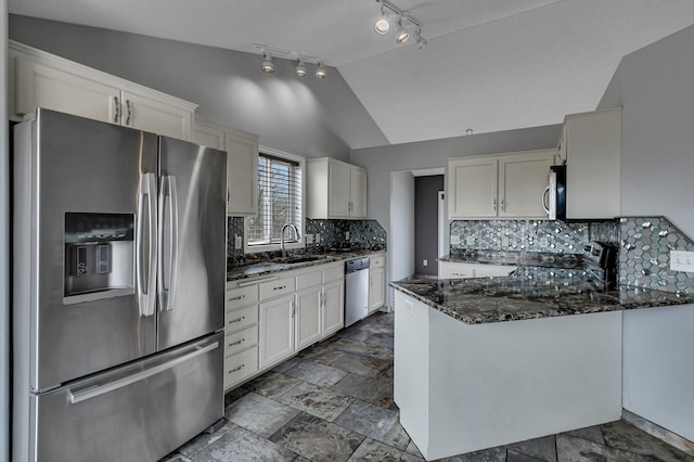 kitchen with a sink, dark stone countertops, stainless steel appliances, white cabinets, and vaulted ceiling