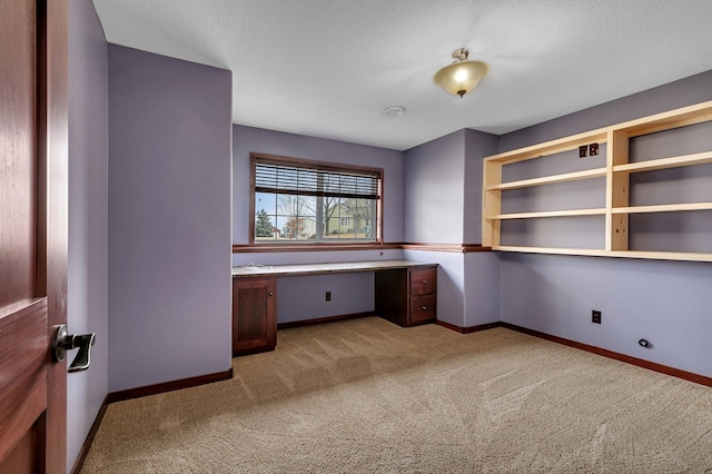 unfurnished office featuring a textured ceiling, carpet, baseboards, and built in study area