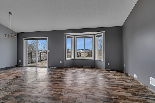 unfurnished room with wood finished floors, visible vents, baseboards, lofted ceiling, and a textured ceiling