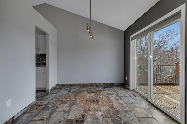 unfurnished dining area with lofted ceiling, stone finish floor, and baseboards