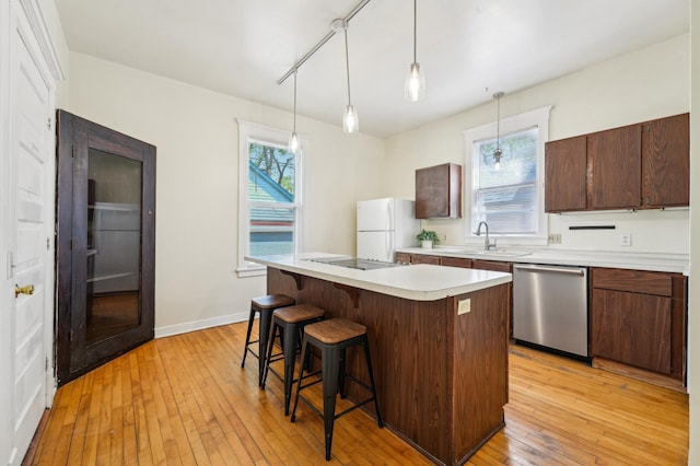 kitchen with dishwasher, freestanding refrigerator, a sink, a kitchen breakfast bar, and light wood finished floors