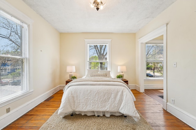 bedroom featuring multiple windows, wood finished floors, a textured ceiling, and baseboards