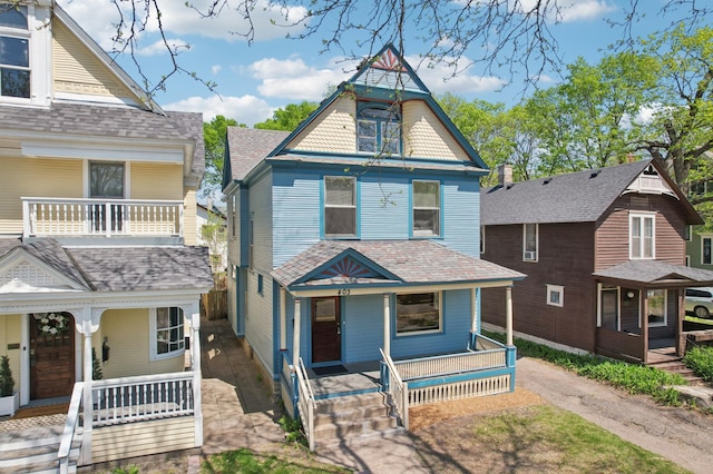 victorian house featuring a porch, roof with shingles, and a balcony