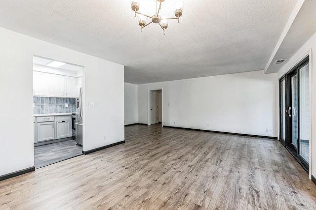 6417 Colony Way Unit 2A, Edina, MN 55435 - unfurnished living room with visible vents, baseboards, a textured ceiling, a notable chandelier, and light wood-type flooring