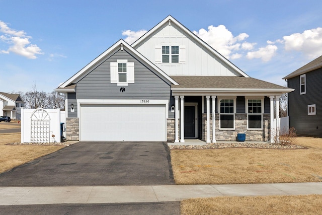 view of front of house featuring driveway, stone siding, fence, covered porch, and board and batten siding