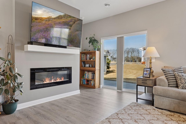 living room with a glass covered fireplace, wood finished floors, and baseboards