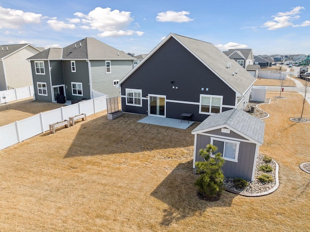 back of property with a lawn, an outbuilding, a fenced backyard, a residential view, and a patio area