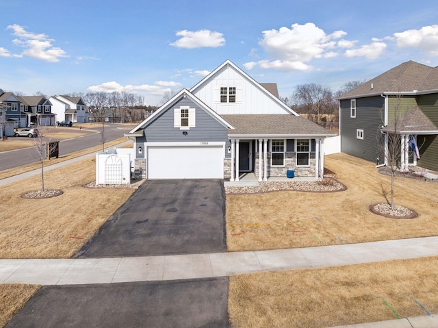 view of front of property with board and batten siding, a front yard, a garage, stone siding, and driveway