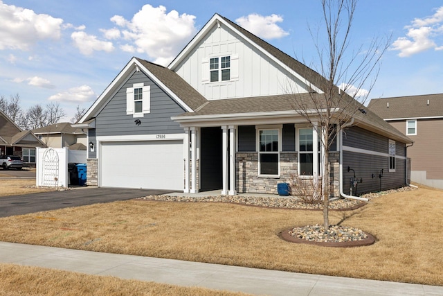 view of front facade with board and batten siding, aphalt driveway, a front yard, a garage, and stone siding