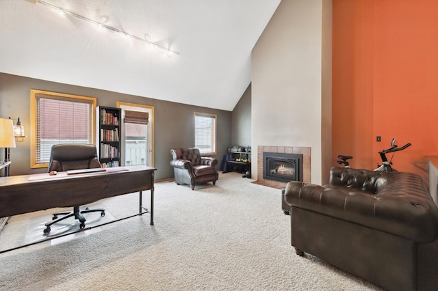 office featuring high vaulted ceiling, track lighting, a tiled fireplace, carpet floors, and baseboards