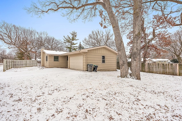 snow covered house with fence and a garage