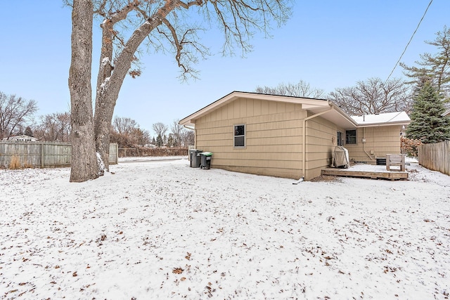 snow covered rear of property with a deck and fence