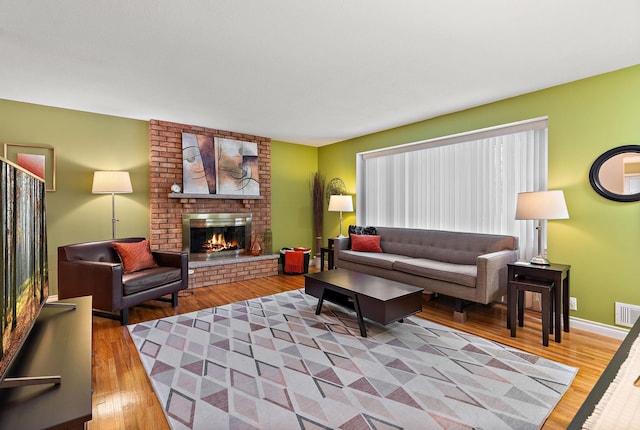 living area with a brick fireplace, wood finished floors, visible vents, and baseboards