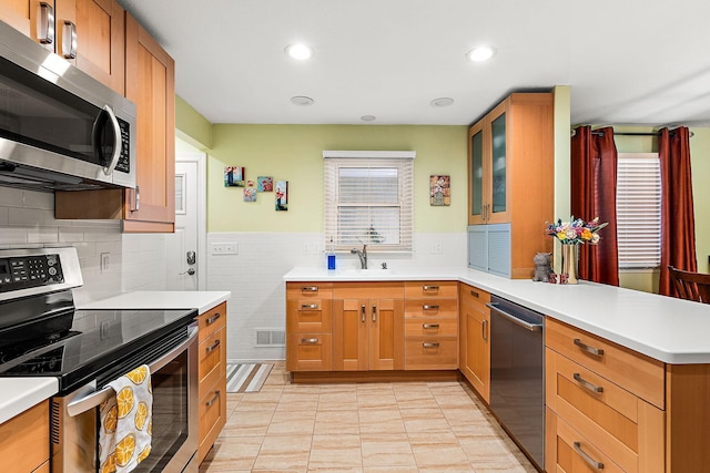 kitchen with glass insert cabinets, light countertops, appliances with stainless steel finishes, a peninsula, and a sink