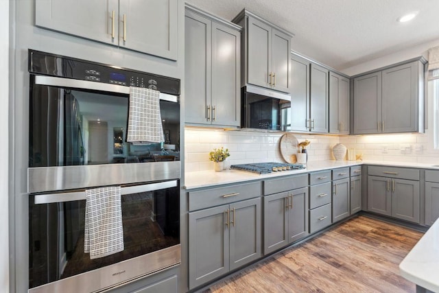 kitchen featuring gray cabinetry, backsplash, wood finished floors, appliances with stainless steel finishes, and light countertops