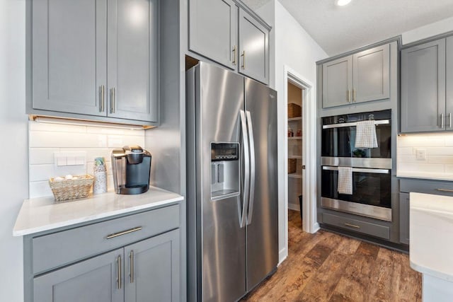 kitchen with decorative backsplash, dark wood-type flooring, appliances with stainless steel finishes, and gray cabinets