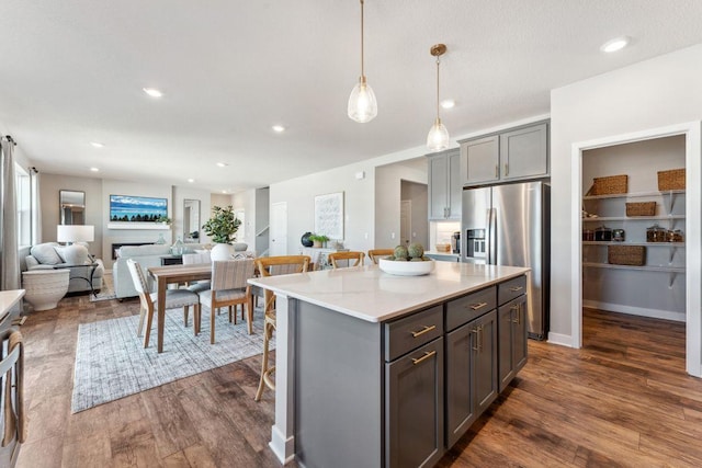 kitchen featuring gray cabinetry, a center island, a breakfast bar, stainless steel fridge, and dark wood-style flooring
