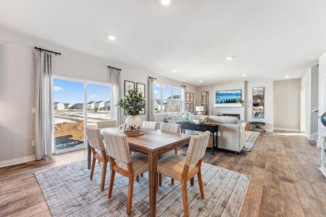 dining area featuring a fireplace, a textured ceiling, baseboards, and wood finished floors