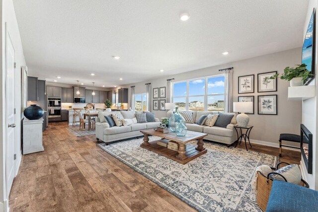 living area featuring recessed lighting, wood finished floors, baseboards, and a textured ceiling