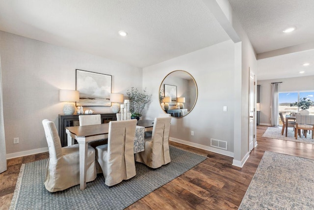 dining area featuring visible vents, baseboards, a textured ceiling, and wood finished floors