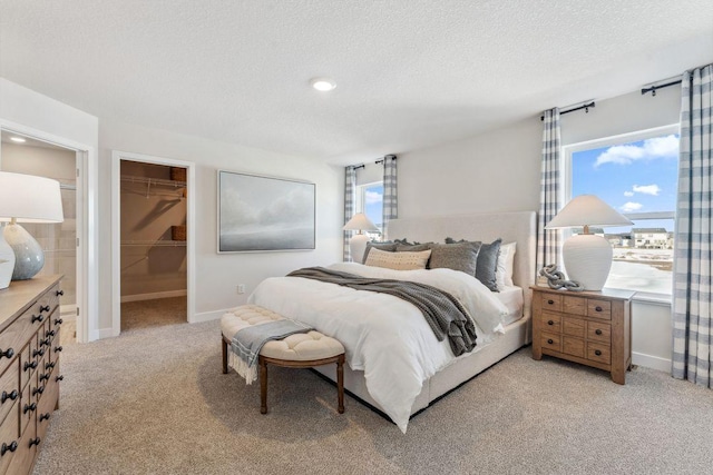 bedroom with a textured ceiling, a closet, baseboards, light colored carpet, and a spacious closet