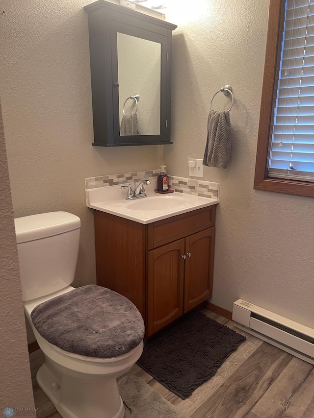 bathroom with toilet, a baseboard heating unit, wood finished floors, decorative backsplash, and vanity