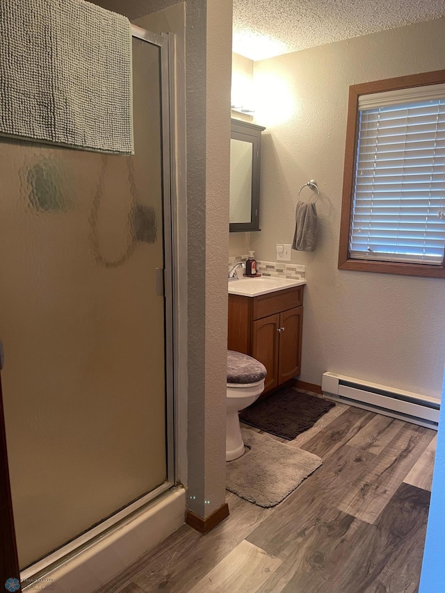 bathroom featuring a shower stall, vanity, baseboard heating, wood finished floors, and a textured ceiling