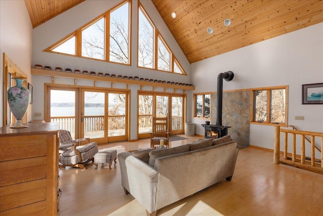 living area featuring high vaulted ceiling, wooden ceiling, a wood stove, and light wood finished floors