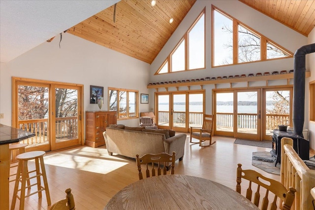 dining room featuring high vaulted ceiling, wooden ceiling, a wood stove, and light wood finished floors