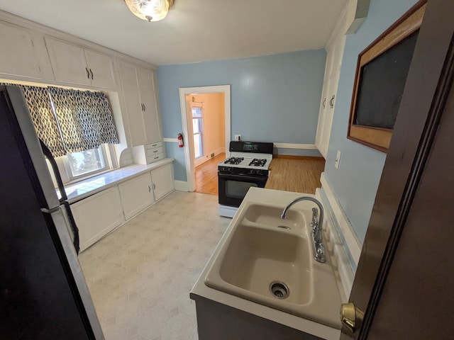 2309 Buchanan St NE, Minneapolis, MN 55418 - kitchen featuring range with gas cooktop, light floors, freestanding refrigerator, white cabinetry, and a sink