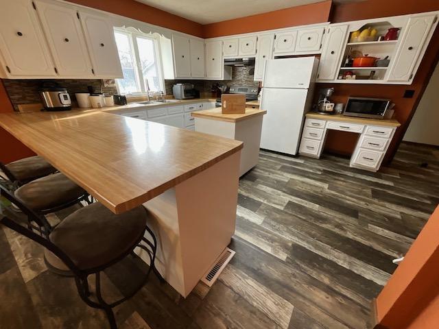 kitchen with stainless steel microwave, dark wood finished floors, white cabinetry, freestanding refrigerator, and a peninsula