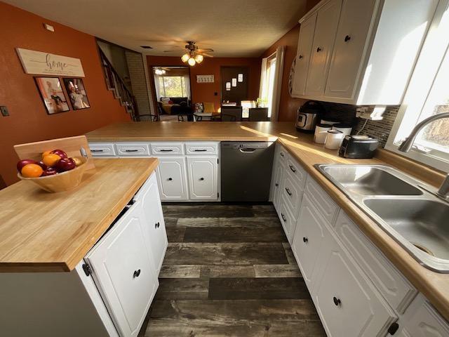 kitchen with dishwashing machine, a ceiling fan, a sink, white cabinetry, and butcher block counters