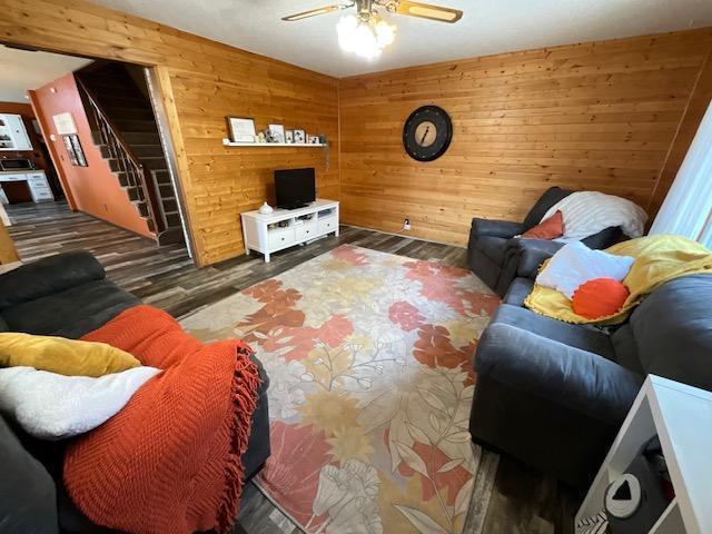 living area featuring wooden walls, stairs, ceiling fan, and wood finished floors