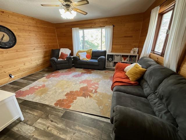 living room with wood walls, a ceiling fan, and wood finished floors