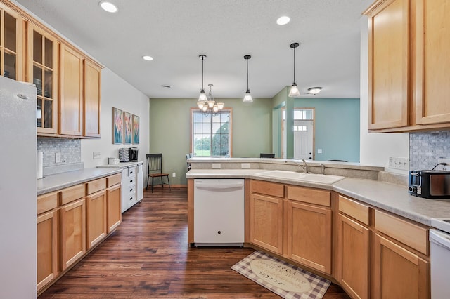 kitchen with backsplash, glass insert cabinets, a peninsula, white appliances, and a sink