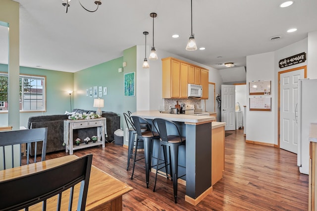 kitchen featuring white appliances, a peninsula, light brown cabinetry, a kitchen breakfast bar, and backsplash