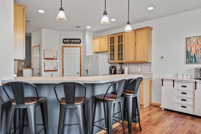 kitchen with backsplash, light brown cabinets, glass insert cabinets, a kitchen breakfast bar, and white fridge with ice dispenser