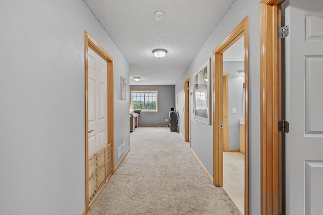 corridor with visible vents, baseboards, light colored carpet, and a textured ceiling