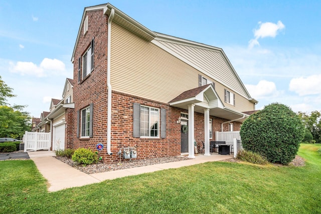 view of front of property featuring a front lawn, fence, cooling unit, a garage, and brick siding