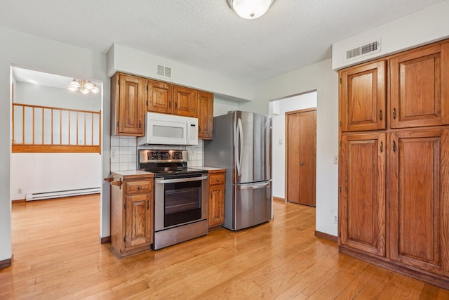 2605 Forest St, Maplewood, MN 55109 - kitchen featuring stainless steel appliances, baseboard heating, brown cabinets, light wood-style flooring, and tasteful backsplash