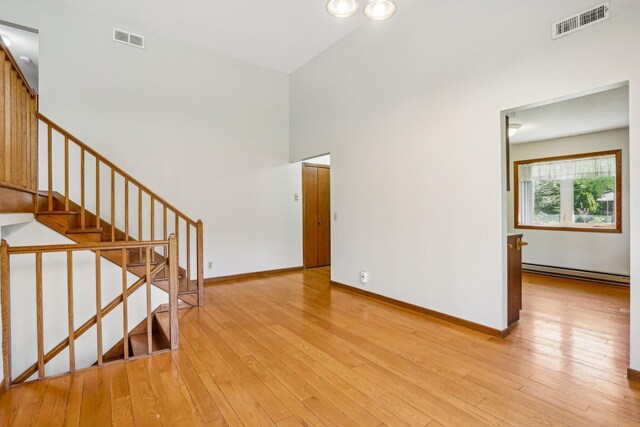 2605 Forest St, Maplewood, MN 55109 - unfurnished living room with a baseboard heating unit, light wood-style floors, baseboards, and a high ceiling