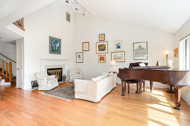 living room with light wood-style floors, a fireplace with flush hearth, stairs, high vaulted ceiling, and rail lighting