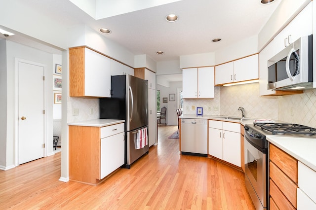 kitchen with appliances with stainless steel finishes, a sink, light countertops, and white cabinetry