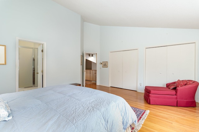 bedroom featuring two closets, wood finished floors, and high vaulted ceiling