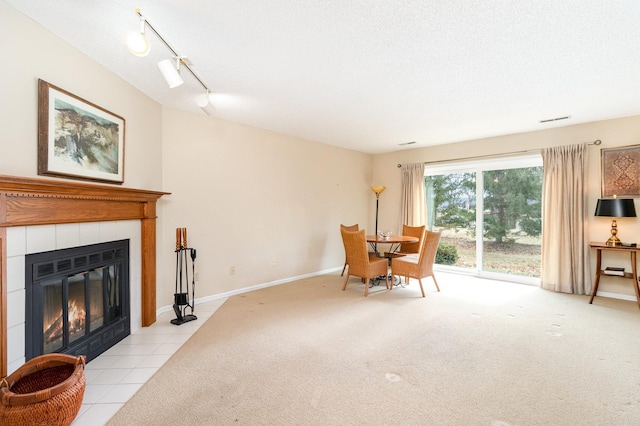 dining room featuring rail lighting, light colored carpet, light tile patterned flooring, a tiled fireplace, and baseboards