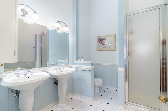 bathroom with a shower stall, toilet, and a wainscoted wall