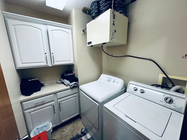 clothes washing area featuring water heater, washer and dryer, cabinet space, and a textured ceiling